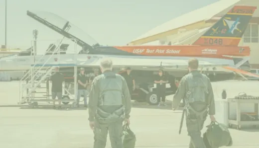  Two military personnel in uniform approach an AI-powered F-16 on the runway.